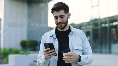 Smiling young attractive bearded man walking use smartphone look around at city Stock Footage 199262087