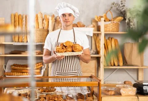 Smiling young baker offering freshly baked croissants Photos