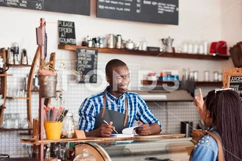 Smiling young barista talking to a customer in his cafe Stock Photos