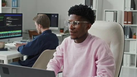 Smiling Young Black IT Professional Sitting at Computer Desk in Office Stock Footage 330124776