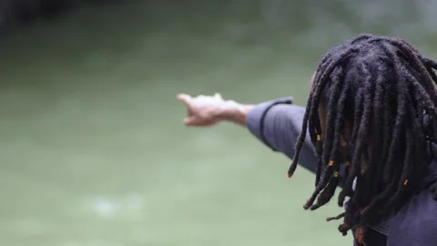 A Smiling Young Black Man Pointing to a Natural Shaped Hole Near a River Stock Footage 207719388