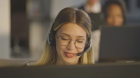 Smiling young blonde speaking with client via headset. Business call. 스톡 동영상 164410244