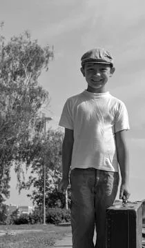 Smiling young boy in flat cap holding vintage suitcase ready for travel Stock Photos