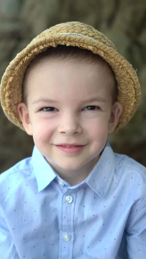 Smiling young boy in a straw hat and blue dotted shirt looks happily Vídeo Stock 347101840