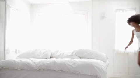 Smiling young couple holding hands jump onto a bed and laugh as they bounce and Vídeos de archivo 88438266