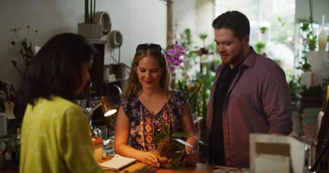 Smiling young couple purchasing a beautiful orchid with a credit card in interio Video stock 199459596