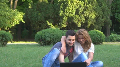 Smiling young couple using computer in park 스톡 동영상 23907305