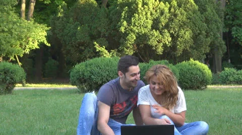 Smiling young couple using computer in park 스톡 동영상 23907728