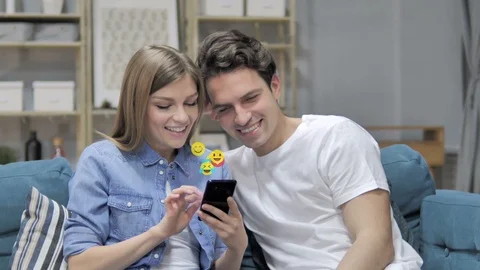 Smiling Young Couple Using Smartphone, Flying Smileys, Emojis and Likes Video stock 112353648