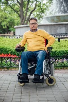 Smiling young disabled man use phone on a wheelchair in a park at sunlight ou Fotos Stock