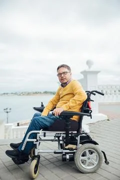 Smiling young disabled man use phone on a wheelchair in a park at sunlight Stock Photos