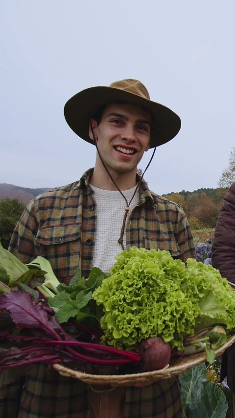 Smiling Young Farmer in Straw Hat Presenting Fresh Organic Produce at a Local Stock Footage 265944639