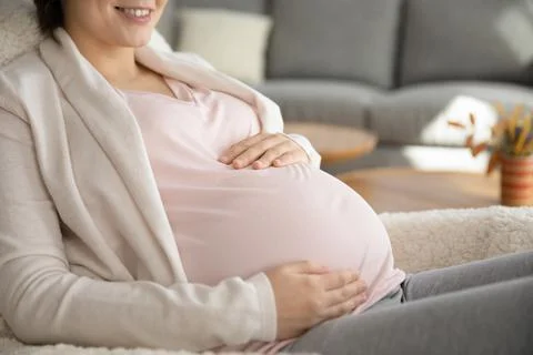 Smiling young female future mom holding hands on pregnant belly Stock Photos