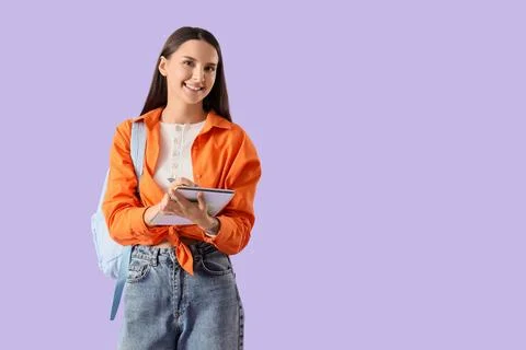 Smiling young female student with backpack and notebook writing notes, educat Stock Photos