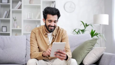 A smiling young freelancer is using, browsing a tablet while sitting on sofa  Stock Footage 252205161