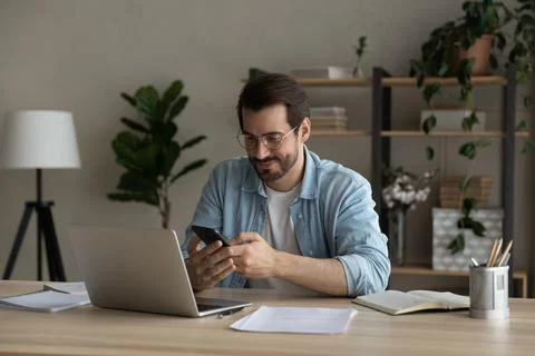 Smiling young guy synchronize data between home computer and smartphone Stock Photos