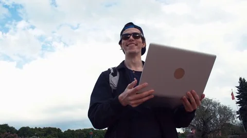 Smiling young hipster using laptop standing at park. Summer day Stock Footage 77168291