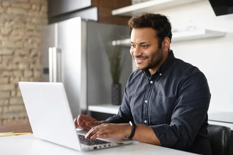 Smiling young indian guy using a laptop for remote work from home Stock Photos