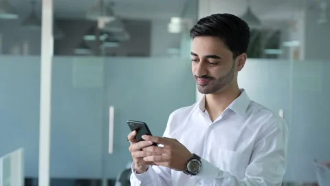 Smiling young Indian man using smart phone and happily texting messages. Видео 170176938
