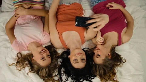 Smiling young ladies taking selfies while laying on the bed after great pajama Stock Footage 73819615