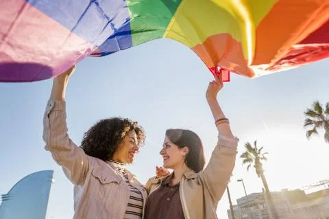 Smiling young lesbian couple waves a rainbow flag Stock Photos