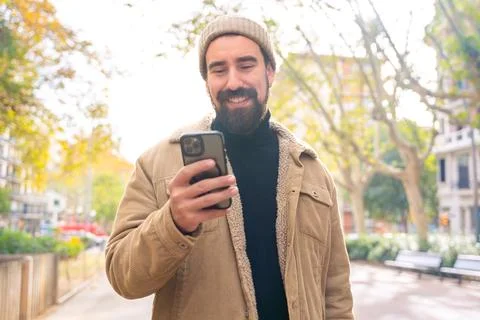 A smiling young man is browsing the internet with a smartphone outdoors. Stock-Fotos