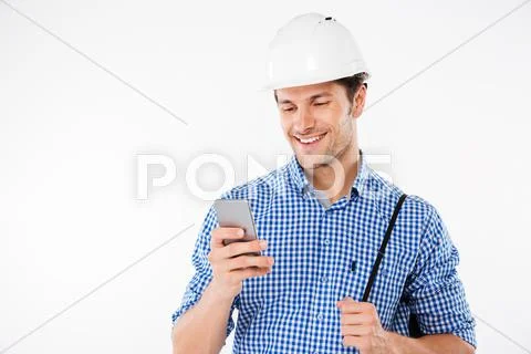 Smiling young man builder in hard hat using mobile phone Stock Photos
