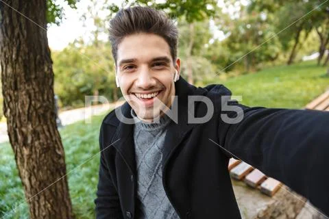 Smiling young man in casual clothing walking outdoors in green park take a se Stock Photos