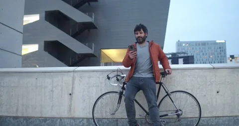 Smiling young man chatting on a mobile phone next to a bicycle in a city Stock Footage 152100507
