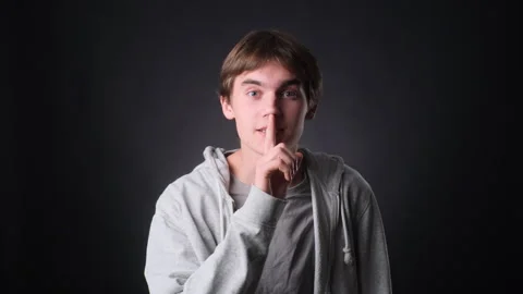 Smiling Young Man with Finger to Lips on black Background Stock Footage 257449648