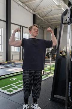 Smiling young man flexing biceps beside strength training machine in bright Fotos Stock