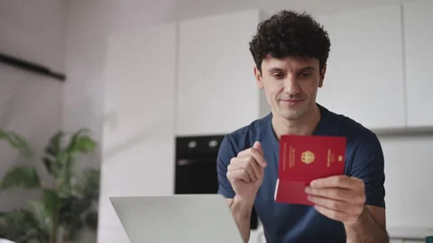 Smiling young man with German passport booking flight tickets on laptop at home Stock Footage 337907357