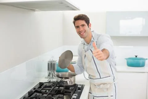 Smiling young man gesturing thumbs up in kitchen Stock Photos