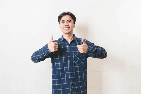 Smiling young man giving two thumbs up on a plain background, expressing ap.. Stock Photos