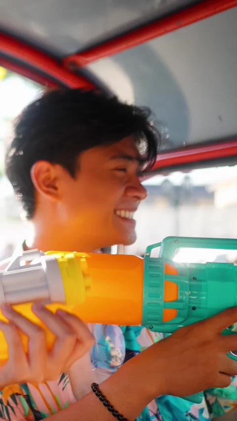 Smiling Young Man Holding Large Water Gun Inside Three-Wheeled Taxi Stock Footage 336245203