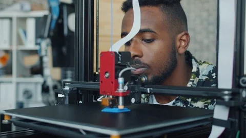Smiling young man looking at 3D printer printing plastic model in office Stock Footage