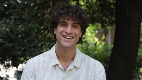 Smiling young man looking at camera in park Stock Footage 277607991