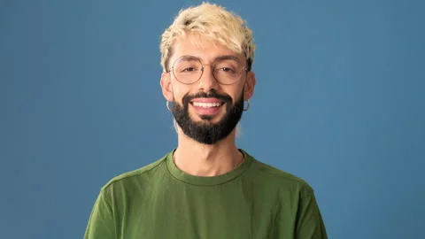 Smiling young man looking at camera, isolated on blue background in a studio Stock Footage 298636923