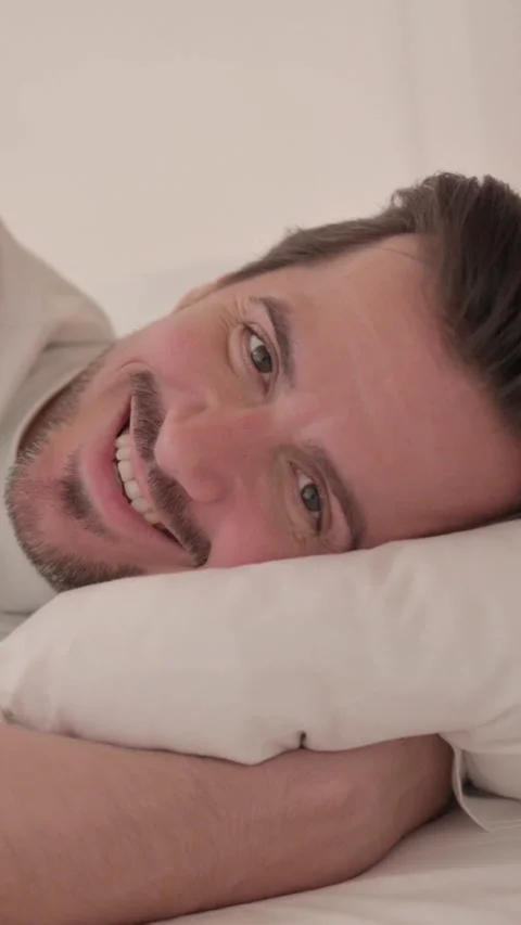 Smiling Young Man Lying in Bed on Side, vertical video Video stock 328565112