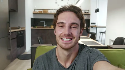 Smiling young man making selfie or video call while sitting at home on sofa Vídeos de archivo 142846426