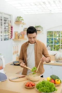 Smiling young man making vegetables salad in the kitchen at home Stock Photos