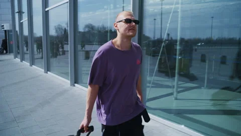 Smiling Young Man in Pink T-Shirt and Cool Sunglasses Pulling Suitcase Outside Video stock 334567313