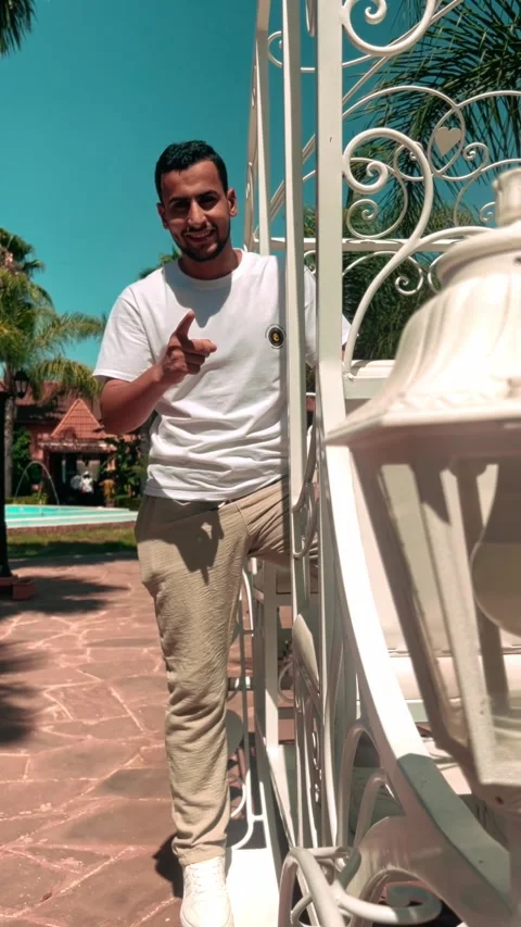 Smiling Young Man Pointing at Camera in Sunny Resort Garden Video stock 318848527