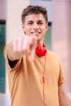 Smiling young man pointing at camera wearing red headphones outdoors.Vertical Stock Photos