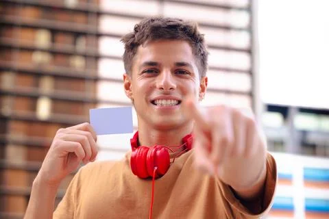 Smiling young man pointing at camera and holding blank business card outdoors Foto stock