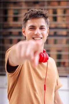 Smiling young man pointing at camera wearing red headphones outdoors.Vertical Stock Photos
