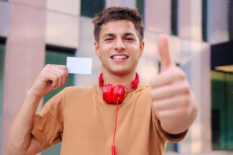 Smiling young man pointing at camera and holding blank business card outdoors Stock Photos