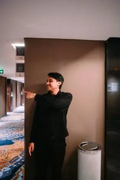 Smiling Young Man Points Way in Modern Building Hallway Foto stock
