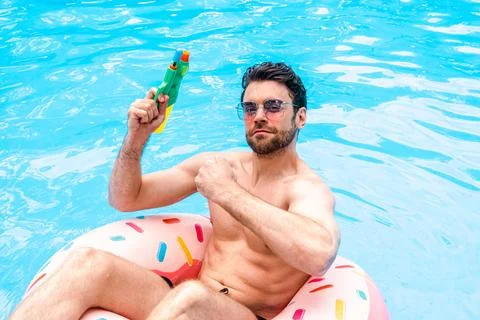 Smiling young man posing at camera while holding toy water gun, resting in the Stock Photos