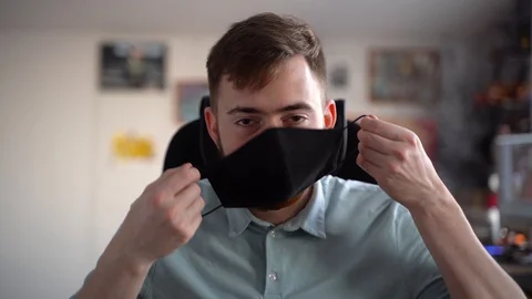 Smiling young man puts on his face a black protective mask Vidéo 127864300
